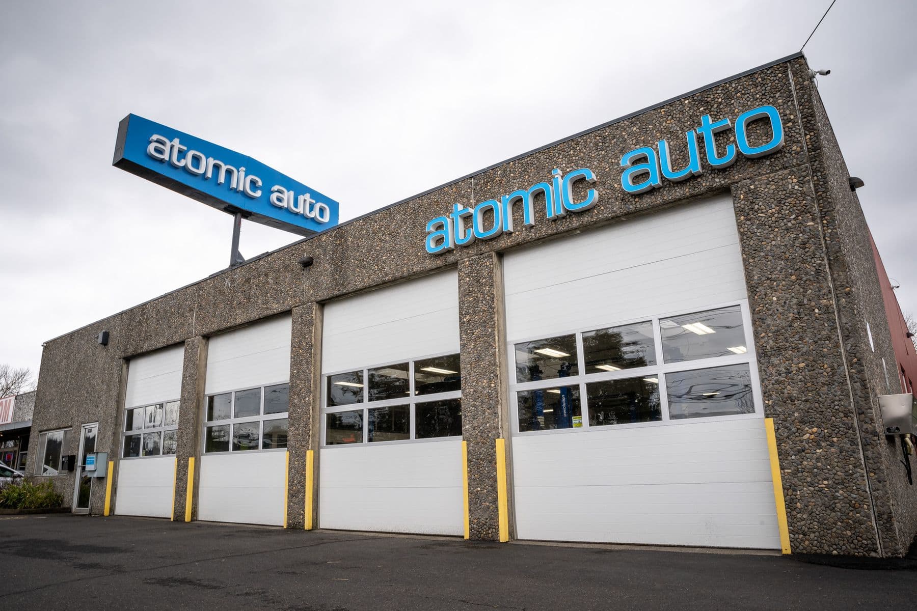 Atomic Auto's four-bay building on NE 102nd Ave, the blue atomic auto sign on the wall and on the pole above it