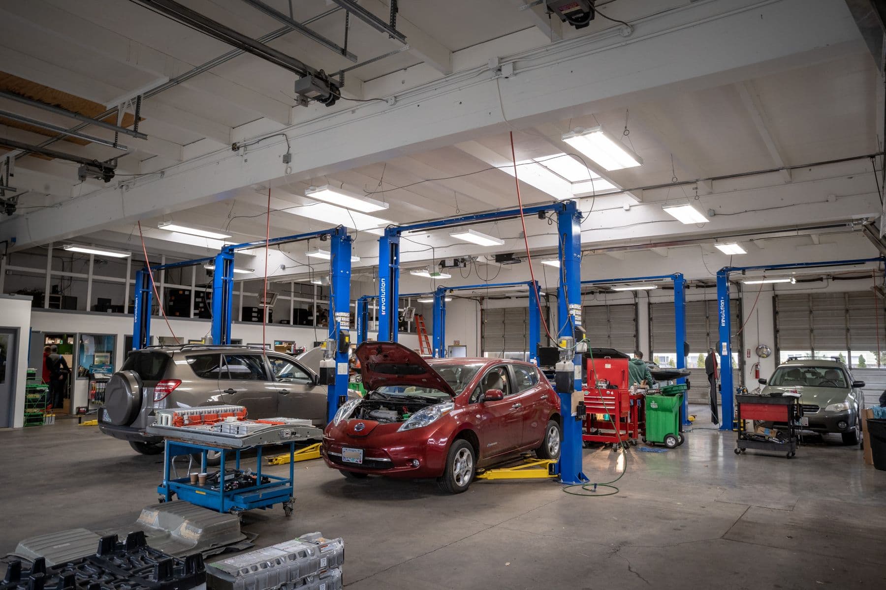 Atomic Auto's shop floor: a red Nissan Leaf with its hood up and a RAV4 on the blue lifts