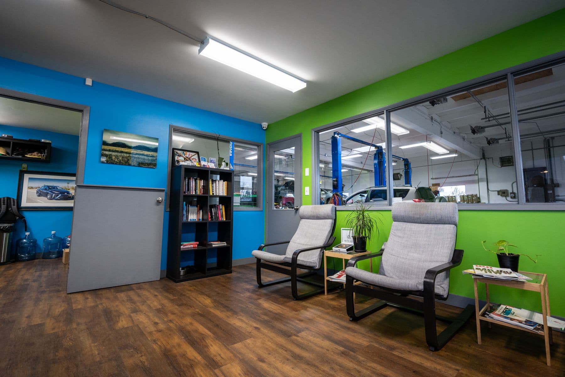 Atomic Auto's waiting room: two armchairs, a bookcase, blue and green walls, and a window onto the shop floor