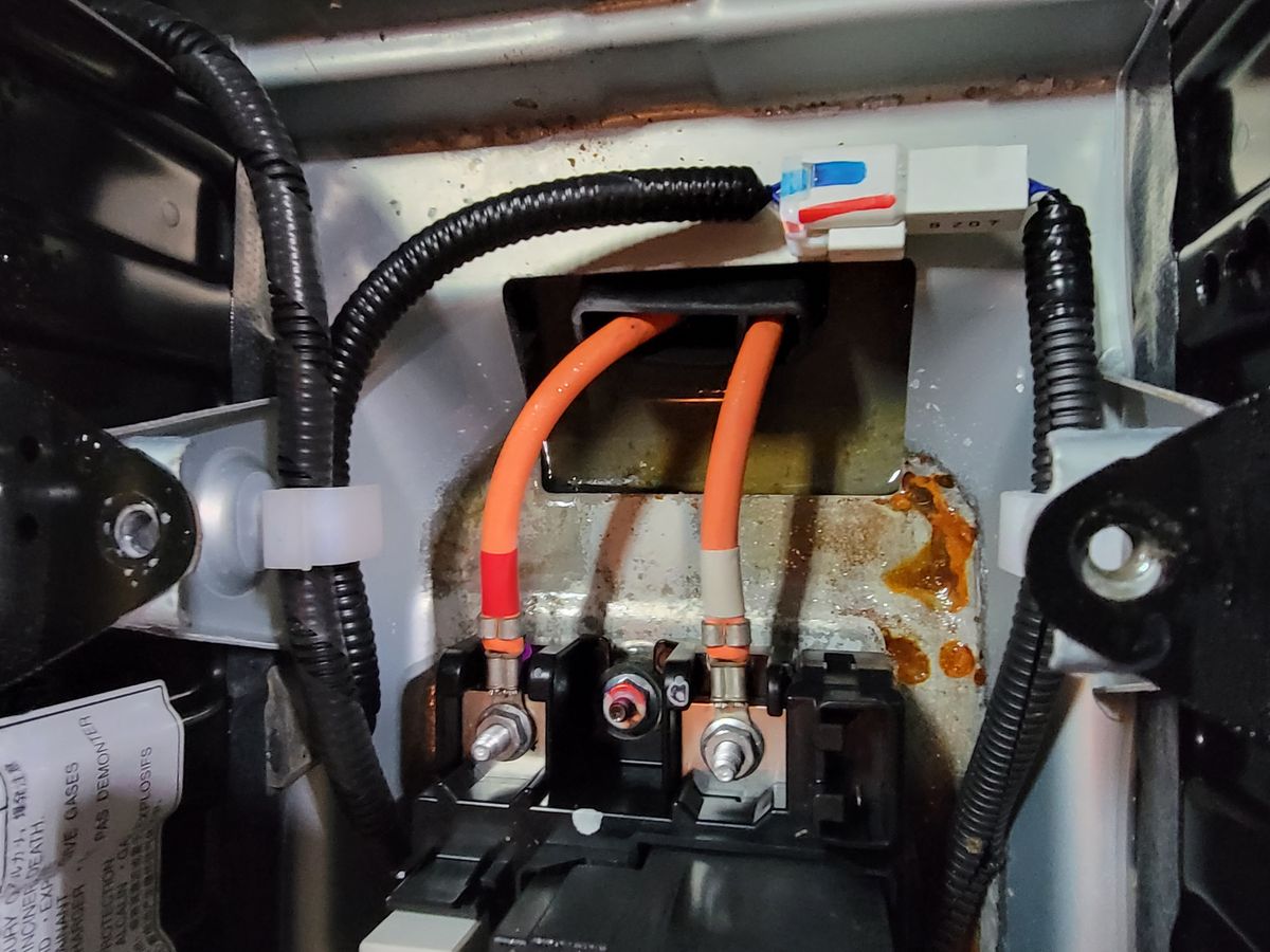 Inside the Highlander Hybrid high-voltage battery, orange HV cables at the relay block with rust-colored water staining pooled in the bottom