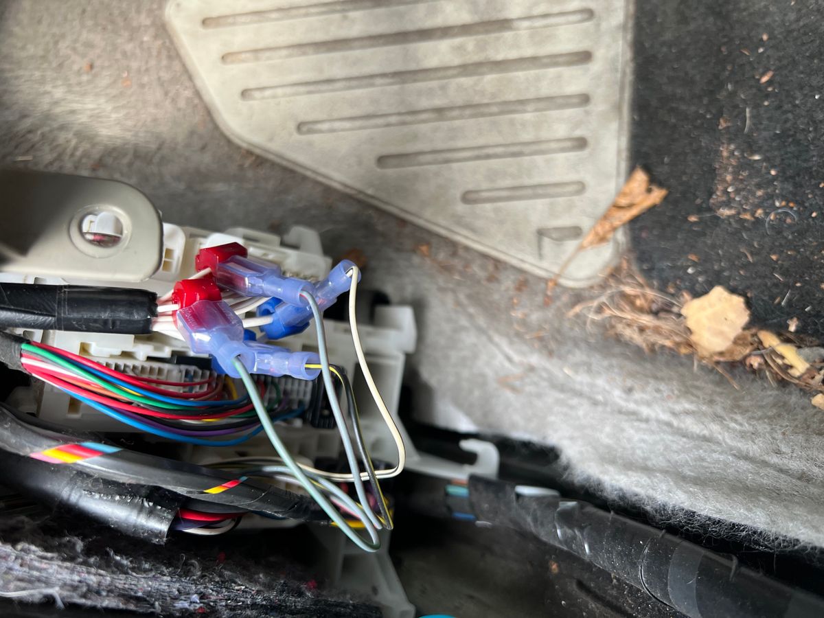 Spliced and taped aftermarket wiring tapped into the factory harness near the kick panel of a 2011 Toyota Prius