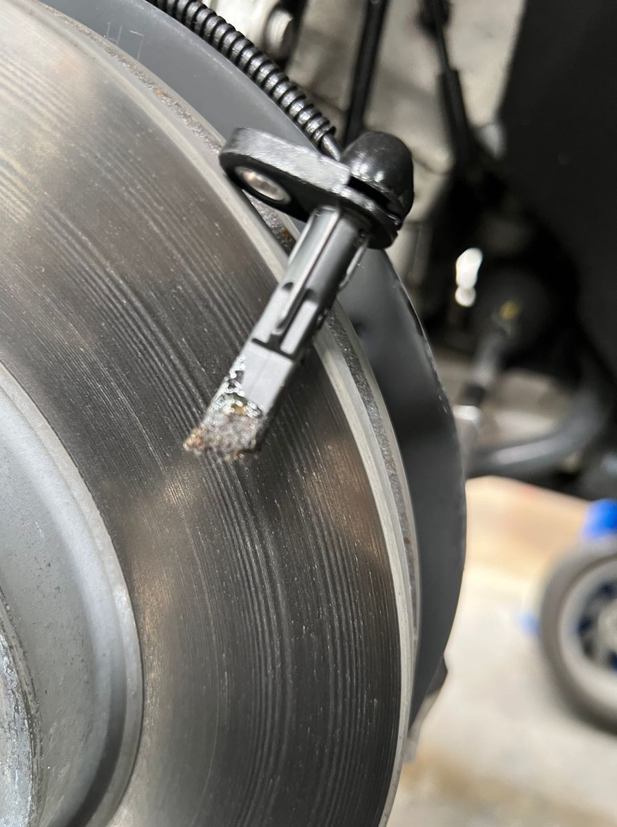 Front wheel speed sensor removed from a 2023 Chevrolet Bolt EUV, its tip caked with metallic debris shed by a deteriorating anti-click washer